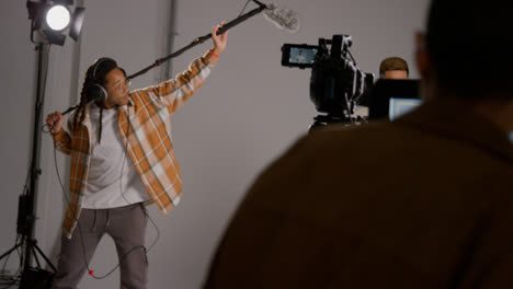 Close-Up-Of-Female-Assistant-Using-Clapperboard-As-Actors-Shoot-Movie-Or-Video-In-Studio-With-Film-Crew-And-Director-Shot-In-Real-Time